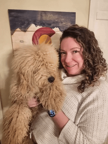 A GIF of a goldendoodle licking a woman's face in joy.